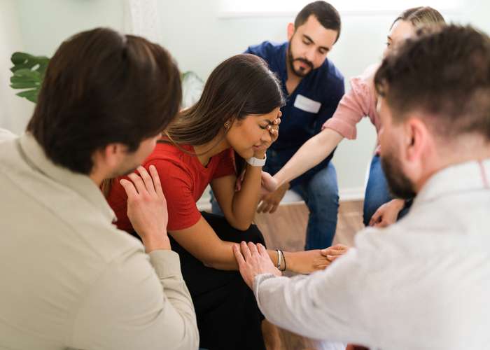 Depressed woman in her 20s crying and receiving support and advice during a group therapy session. Young women and men comforting a sad woman